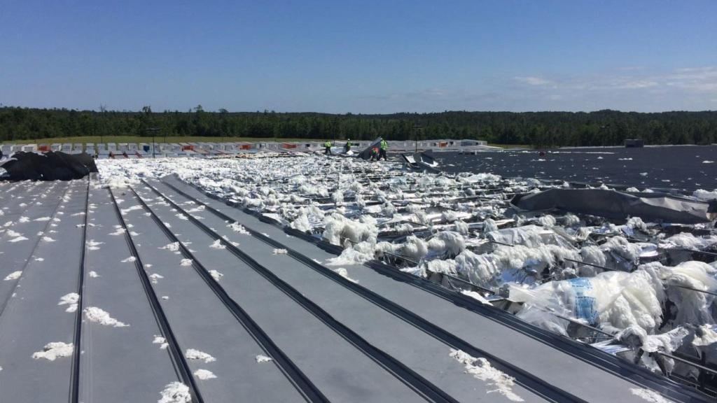 Storm damaged roof with work crew visible in background